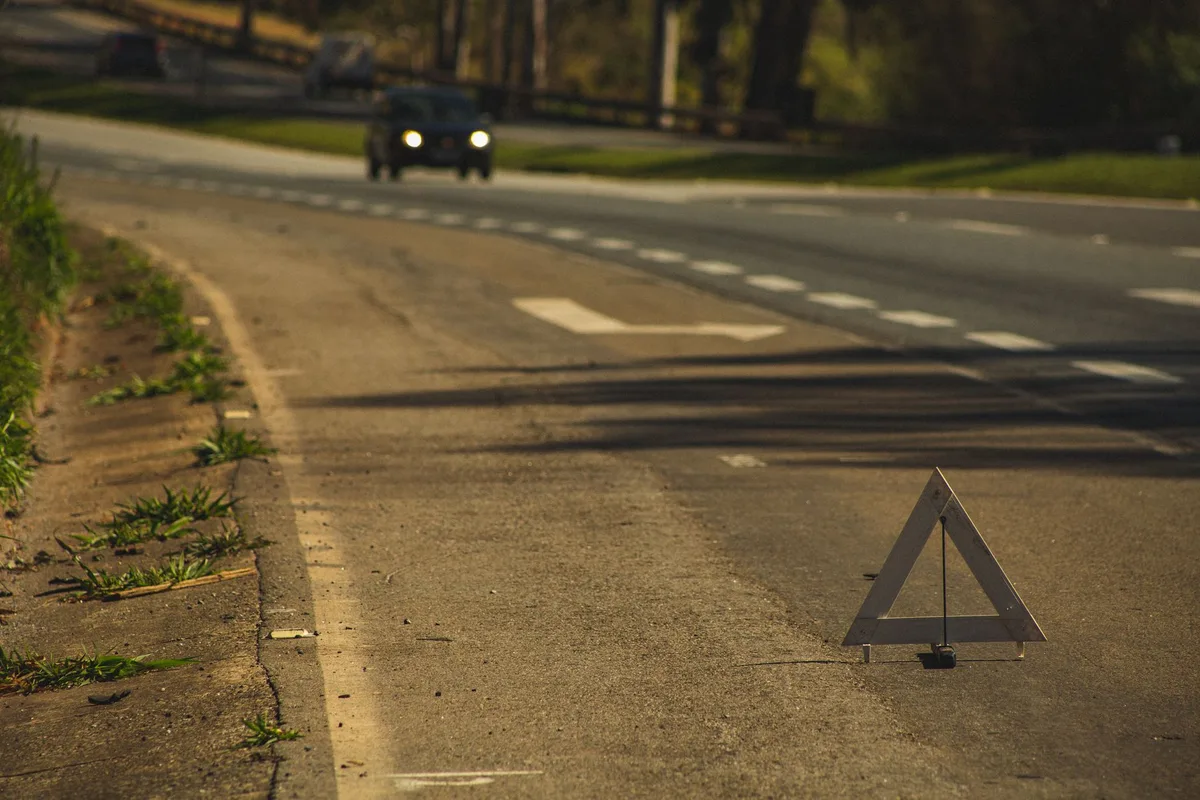 Voiture endommagée en bordure de route avec feux de détresse et triangle de signalisation