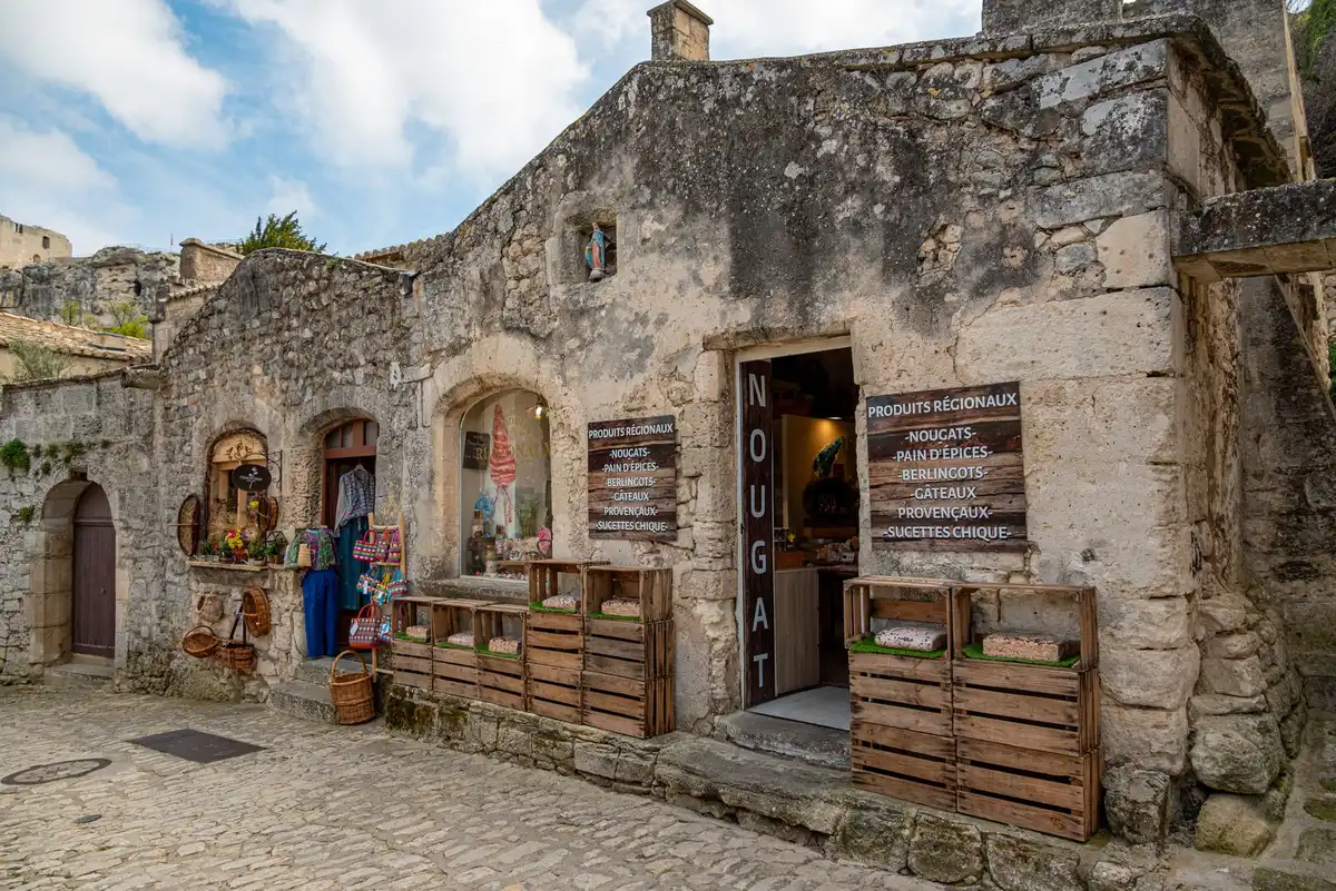 Place ombragée d'un village provençal avec marché local et façades anciennes.