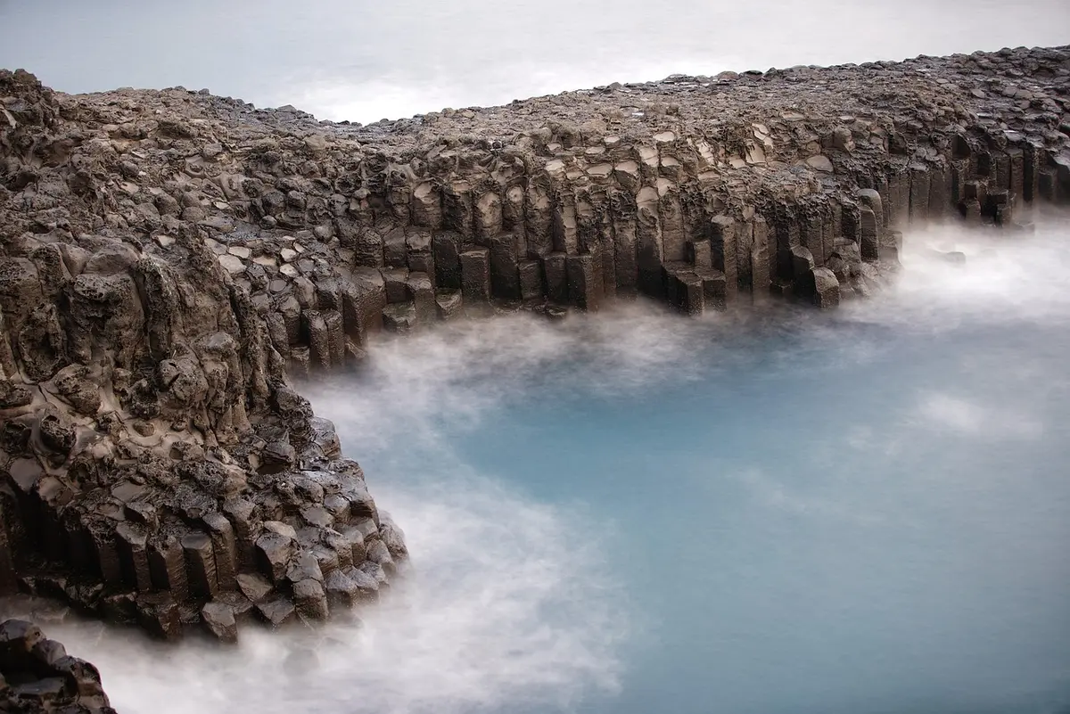 Plage de sable noir volcanique avec colonnes basaltiques et vagues puissantes