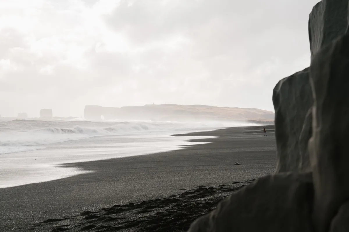 Plage de sable noir encadrée par des rochers et des falaises côtières