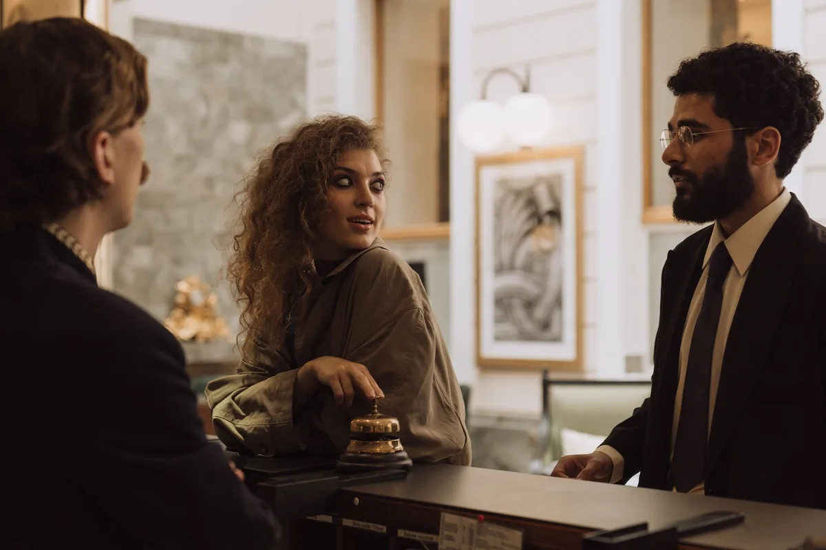 Réception d'hôtel avec personnel accueillant et client discutant de la facturation.