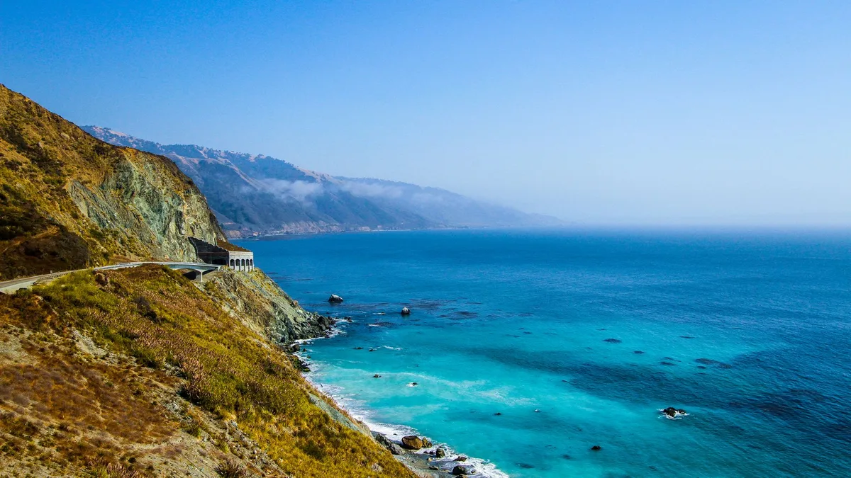 Route côtière californienne avec falaises rocheuses et océan bleu, paysage emblématique de la côte ouest