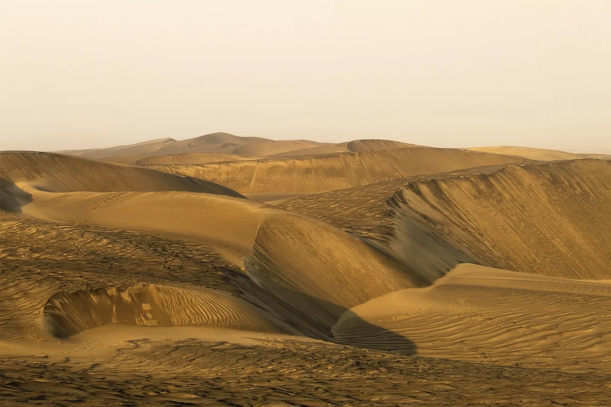 Lever de soleil sur une dune avec randonneurs et voiture garée au loin