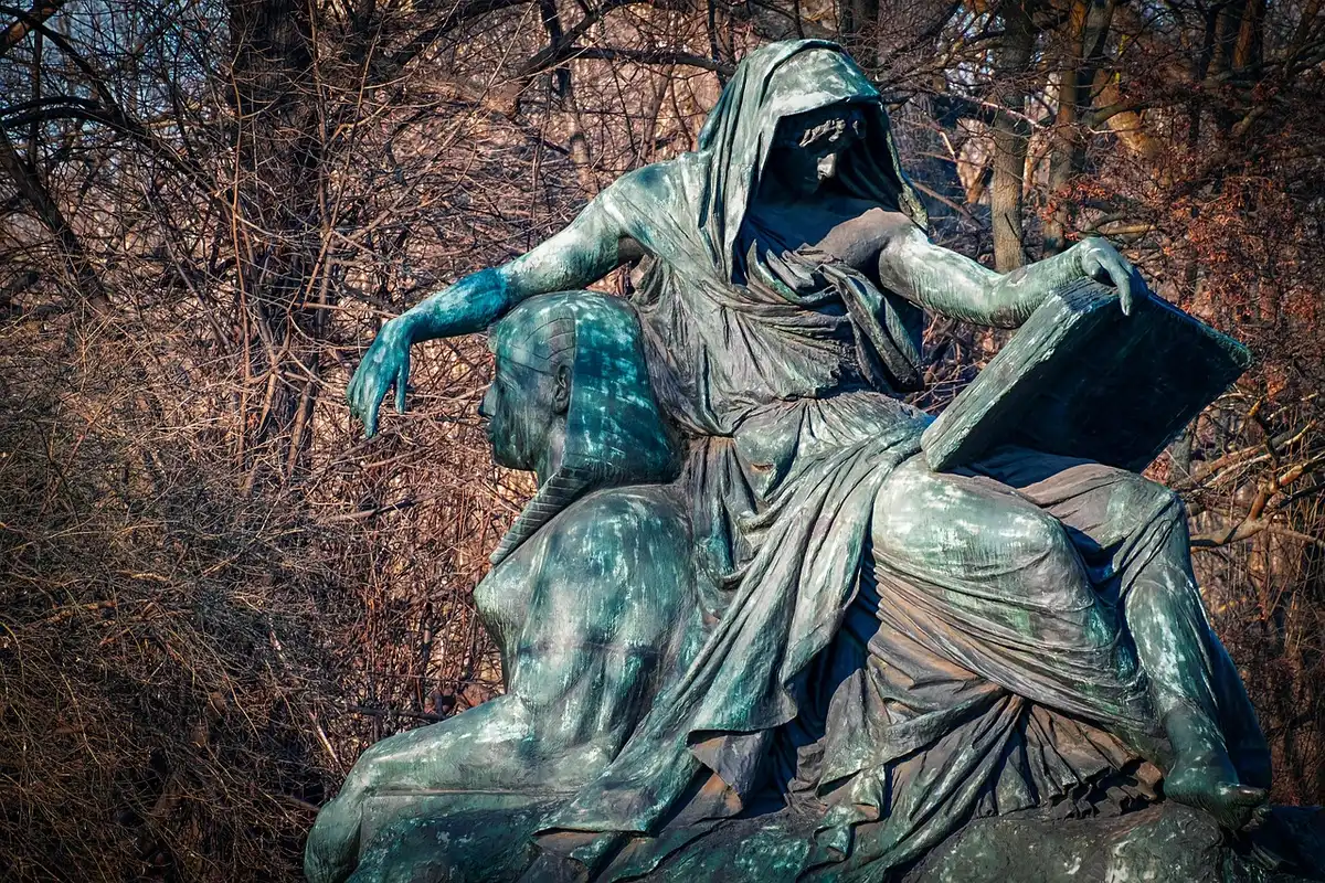 Grande sculpture féminine partiellement recouverte d'herbe au bord d'un lac