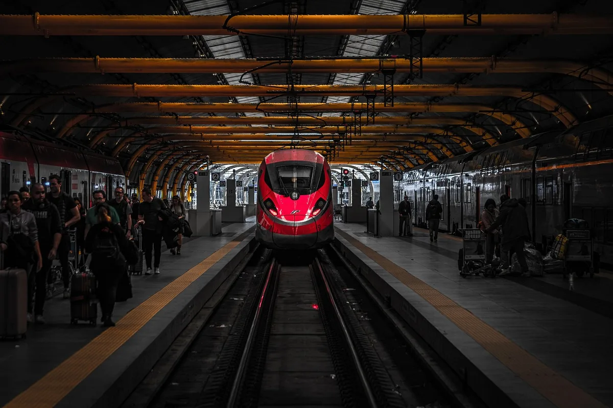 Foule distante sur un quai de gare en journée, trains et panneaux d'arrivée visibles
